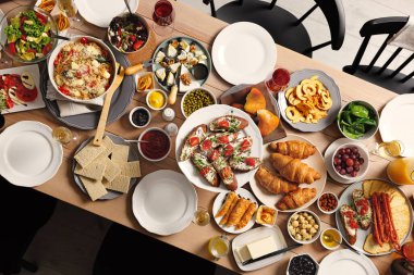 Farklı lezzetli yemek ve sandalyelerle dolu kahvaltı masası, üst manzara.