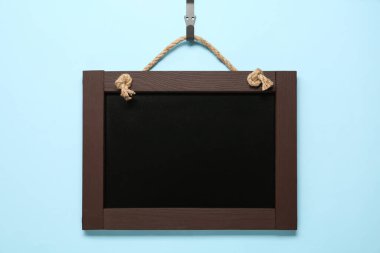 Açık mavi arkaplanda asılı duran temiz küçük siyah karatahta