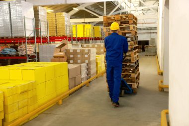 Depoda manuel forkliftle ahşap paletler taşıyan bir işçi.