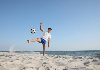 Sahilde futbol oynayan bir adam.
