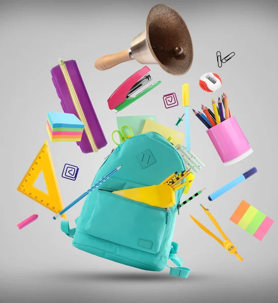 Turquoise backpack, school bell and different stationery flying on light grey background