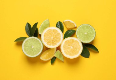 Taze limonlar, limonlar ve yeşil yapraklar sarı arka planda, düz yerde.