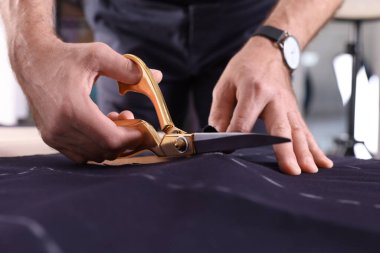 Profesyonel terzi masadaki tebeşirli dikiş kalıbını takip ederek kumaşı kesiyor.