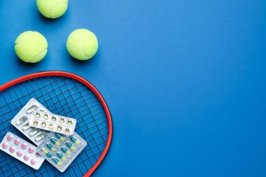 Tenis raketi, toplar ve haplar mavi arka planda, düzlük ve mesaj için boşluk. Doping kavramı