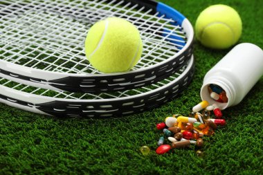 Tenis raketleri, toplar ve yeşil çimlerin üzerinde haplar, yakın plan. Doping kavramı