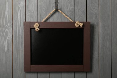 Gri ahşap duvarda asılı temiz, küçük siyah bir karatahta.