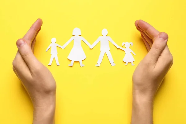 Woman protecting paper cutout of family on yellow background, top view