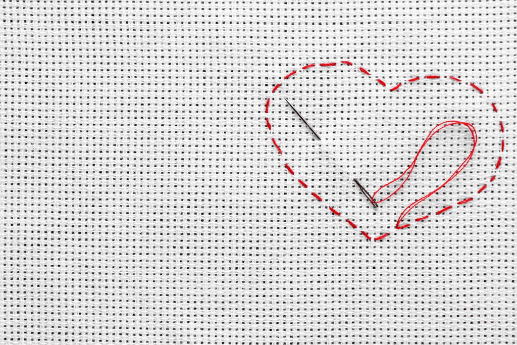 Canvas with embroidered heart and needle as background, top view. Space for text