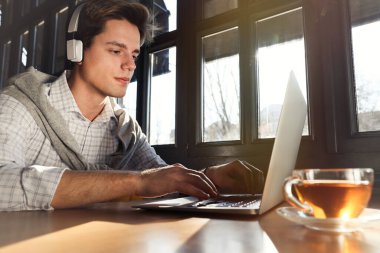 Laptop ve kulaklıklı genç bir öğrenci kafede ders çalışıyor.