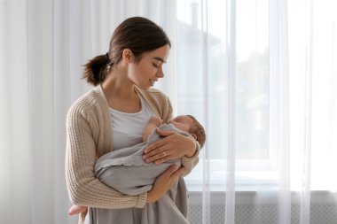 Evinin penceresinin yanında bebeği olan genç bir kadın.