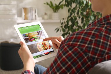 Evde yemek siparişi vermek için tablet kullanan bir adam, yakın çekim. Teslimat servisi