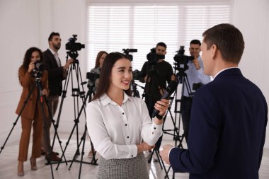 Profesyonel genç gazeteci arka planda iş adamı ve kamera operatörü grubuyla röportaj yapıyor.