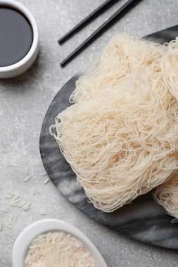 Pişmemiş pirinç eriştesi, soya sosu ve açık gri masada çubuklar.