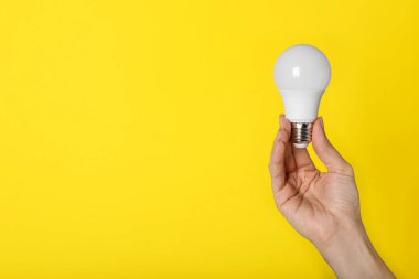 Sarı arka planda LED ampulü tutan kadın, yakın plan. Metin için boşluk