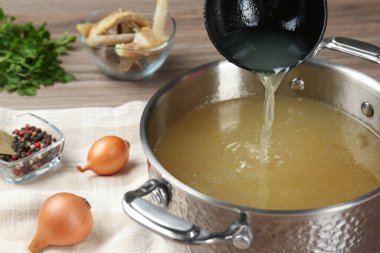 Lezzetli ev yapımı kemik suyu ve ahşap masadaki malzemeler, yakın plan.