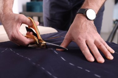 Profesyonel terzi masadaki tebeşirli dikiş kalıbını takip ederek kumaşı kesiyor.