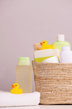 Bebek kozmetik ürünleri, banyo aksesuarları ve gri arka planda beyaz masalarda plastik ördekler olan sepet.