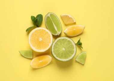 Taze limonlar, limonlar ve nane yaprakları sarı arka planda, düz uzanmış.
