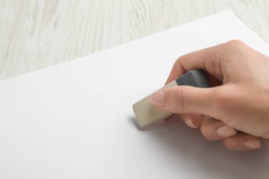 Beyaz ahşap masadaki defterden bir şey silen kadın, yakın plan.