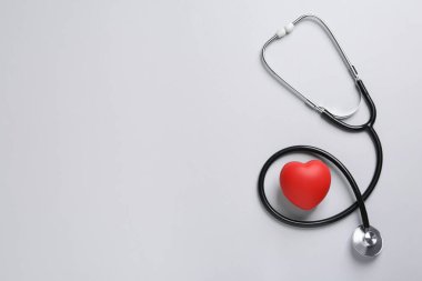 Stetoskop, gri arka planda kırmızı dekoratif kalp, metin için yeri olan düz bir yer. Kardiyoloji kavramı