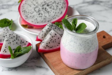 Lezzetli pitahaya smoothie, ejderha meyveleri ve beyaz mermer masada taze nane.