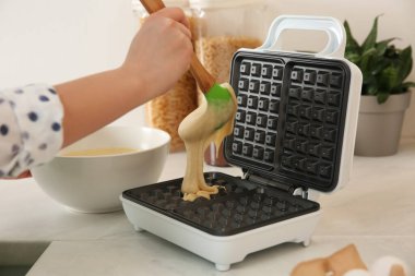 Kadın Belçikalı waffle makinesinin üzerine hamur döküyor.