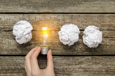 Ahşap masada, kağıt topların arasında ampul tutan bir kadın. Fikir kavramı