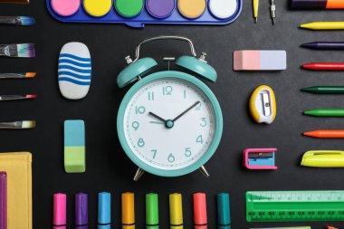 Çalar saat ve tahtada farklı kırtasiye malzemesi olan düz bir kompozisyon. Okul zamanı.