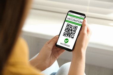 Uluslararası aşı sertifikalı akıllı telefonu olan bir kadın kapalı alanda, yakın plan.