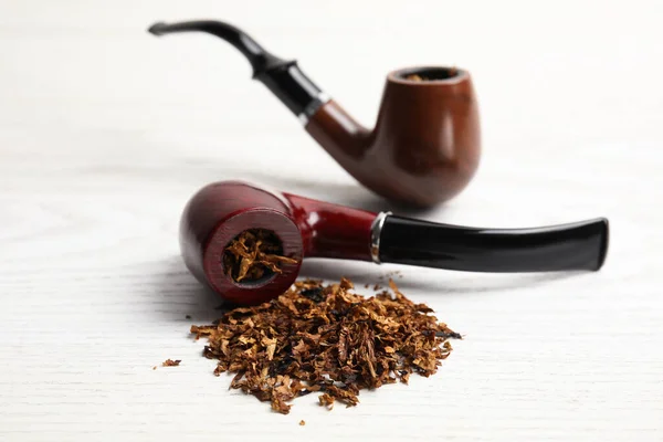 Smoking pipes with tobacco on white wooden table