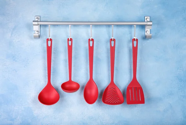 Rack with kitchen utensils hanging on light blue wall
