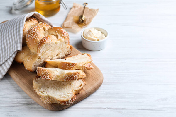 Cut freshly baked braided bread and butter on white wooden table, space for text. Traditional Shabbat challah