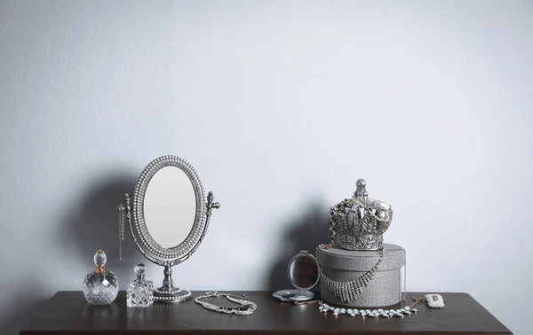 光の壁の近くの木製テーブルの上の小さな鏡 香水瓶や宝石類 — ストック写真