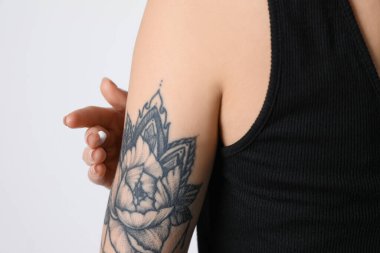 Beyaz arka planda dövmesi olan bir kadın koluna krem sürüyor.