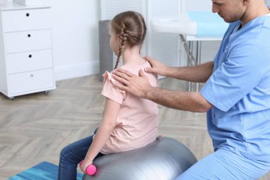 Ortopedist, çocuğun klinikte dambılla egzersiz yapmasına yardım ediyor. Skolyoz tedavisi