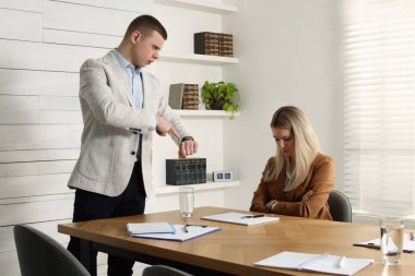 İş adamı, çalışanı ofise geç kaldığı için azarlarken kol nöbetini işaret ediyor.