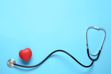 Stetoskop ve açık mavi arka planda kırmızı dekoratif kalp, metin için yeri olan düz bir yer. Kardiyoloji kavramı