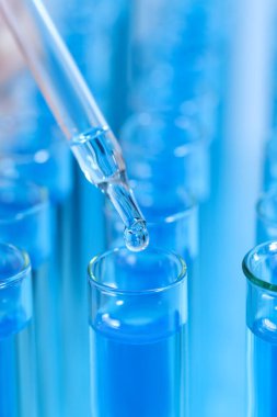 Test tüpüne mavi sıvı damlatılıyor, yakın plan. Laboratuvar analizi