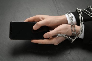 Siyah masada zincire vurulmuş akıllı telefonu tutan adam, yakın plan. İnternet bağımlılığı