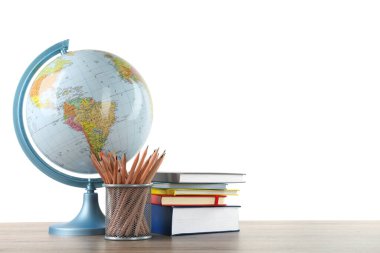 Küre, okul gereçleri ve tahta masanın üzerindeki kitaplar beyaz arka plana karşı. Coğrafya dersi