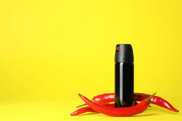Bottle of gas pepper spray and fresh chili peppers on yellow background. Space for text