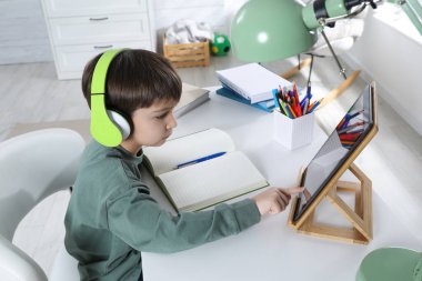 Modern tabletle evde internetten ders çalışan şirin bir çocuk. E-öğrenme