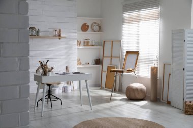 Sanatçının iş yeri ve geniş pencerenin yanında ahşap sehpası olan modern bir stüdyo.