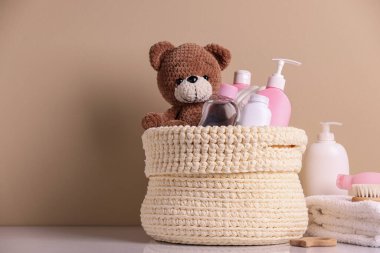 Bej arka planda bebek kozmetik ürünleri, banyo aksesuarları ve oyuncak ayıyla örülmüş sepet. Metin için boşluk