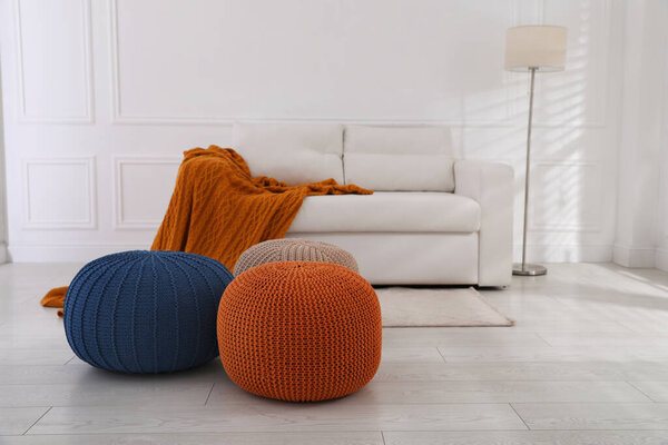 Stylish living room interior with white sofa and knitted poufs