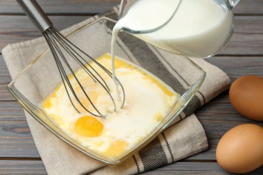 Tahta masada çırpılmış yumurtalara süt ekliyorum. Yakın plan.