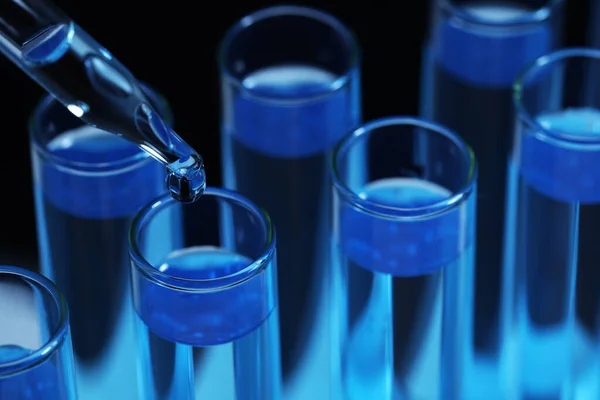 将试剂滴入带有蓝色液体的试管中 在黑色背景上 实验室分析 — 图库照片