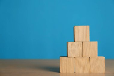 Açık mavi arkaplana karşı tahta masanın üzerindeki boş küp piramidi. Metin için boşluk