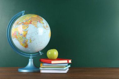 Küre, kitaplar ve elma yeşil karatahtanın yanında, yazı için yer var. Coğrafya dersi
