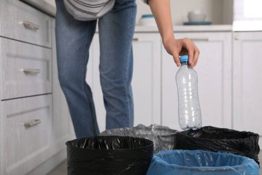 Kadın mutfaktaki çöp kutusuna plastik şişe atıyor, yakın plan. Atık toplamayı ayır